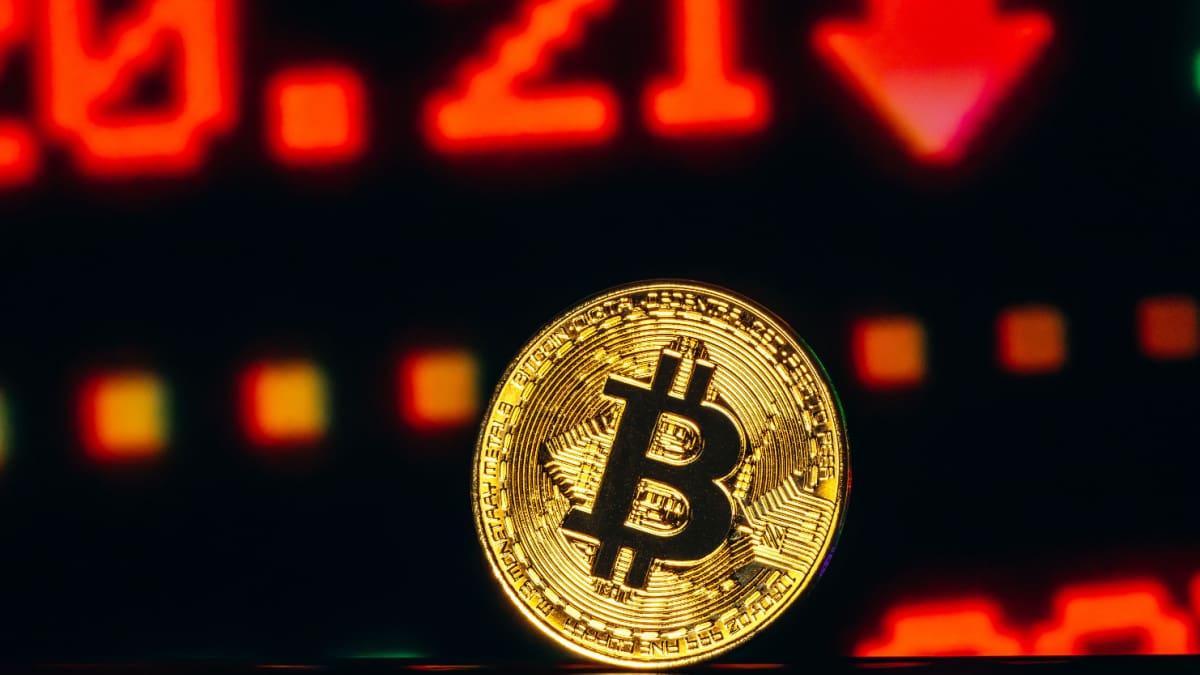 Een afbeelding van een bitcoin (BTC) munt met rode cijfers en een dalende prijs op de achtergrond Een afbeelding van een bitcoin (BTC) munt met rode cijfers en een dalende prijs op de achtergrond